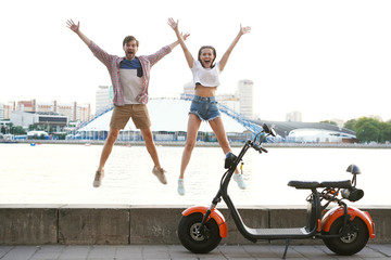 Couple in love jumping, motorbike standing near. Young riders enjoying themselves on trip. Adventure and vacations concept