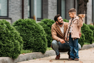 bearded father and smiling son with toy plane looking at each other on street