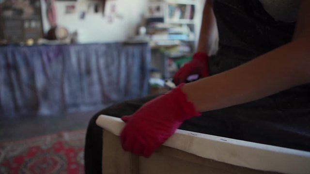 Closeup tracking shot of female painter in apron and gloves using staple gun to stretch canvas on frame in art studio