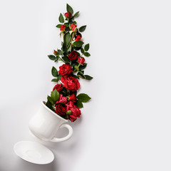Creative layout made of coffee or tea cup with red roses on white background