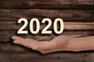 Hand offering 2020 numbers, wood background, new year and holidays greeting card