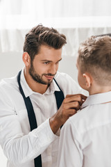 smiling father helping son to get dressed at home