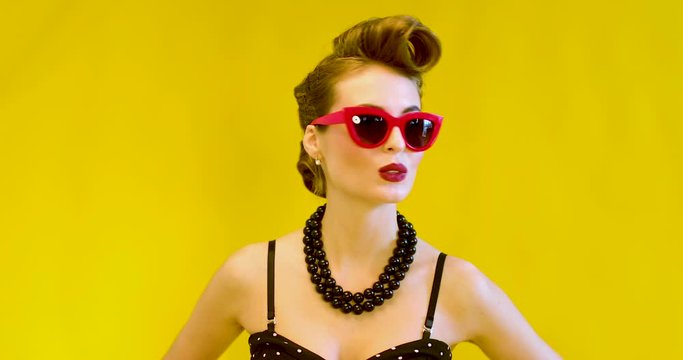 Beautiful glamorous young model with a interesting hairstyle  with sunglasses is posing at studio. Pin-up style in clothes, hair and make-up. 