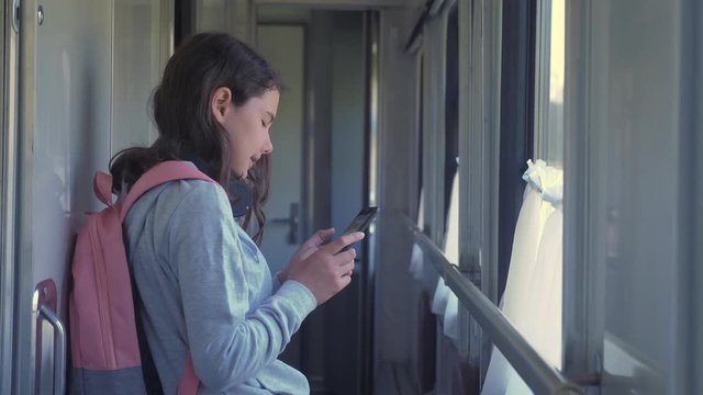 little girl walks on a train compartment car with a backpack and a smartphone. travel transportation railroad concept. the girl in the train lifestyle at the window corresponds the girl in the train