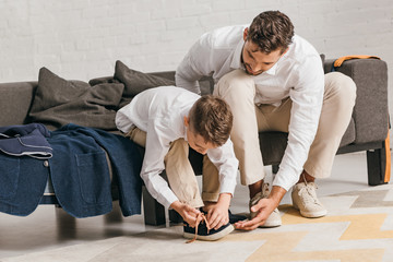 father teaching son to tying shoelaces at home - obrazy, fototapety, plakaty