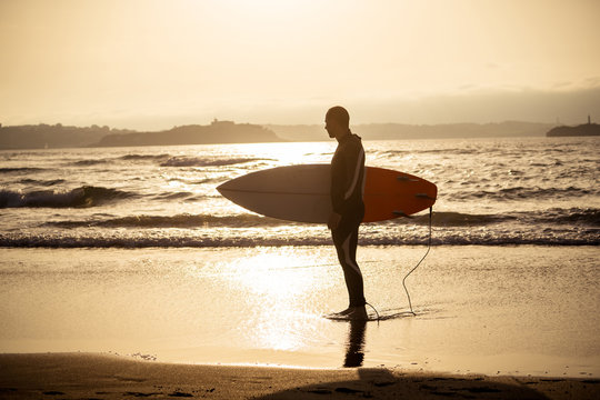 Surfer with surfboard on the beach at sunset or sunrise. Adventure surf advertising image