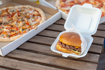 Eating out on summer terrace with italian cheesy pizza and juicy hamburger