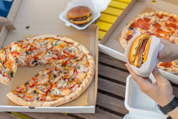 Eating out on summer terrace with italian cheesy pizza and juicy hamburger