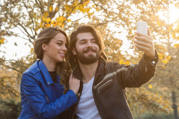 Young couple using cellphone in autumn colored park.