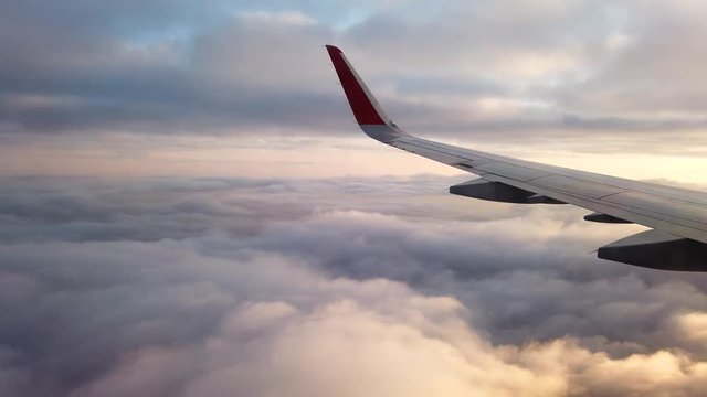 View from the porthole of an airplane. Flying at high altitude over an even layer of clouds. Early morning.