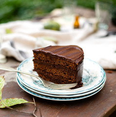 beautiful outdoor still life in autumn garden with tasty slice of chocolate cake on vintage plates stands on rustic wooden table with grey napkin and pumpkins, selective focus