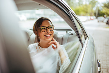 Portrait of a cheerful young woman traveling by a car and looking outside the window.