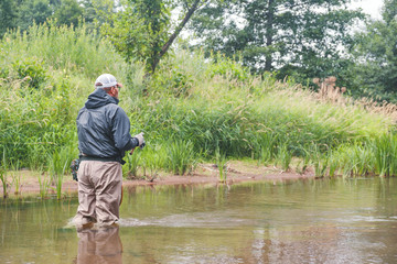 Fishing in the waders. Fisherman on a forest river.