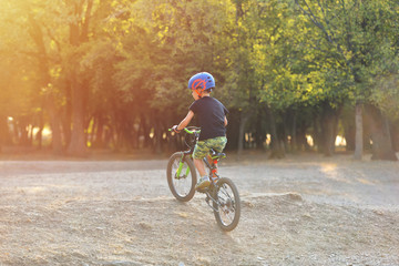 Fototapeta premium Happy kid boy of 7 years having fun in autumn park with a bicycle on beautiful fall day. Active child wearing bike helmet