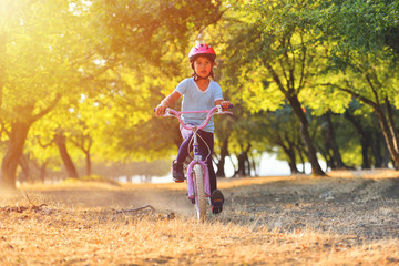 Happy kid girl of 7 years having fun in autumn park with a bicycle on beautiful fall day. Active child wearing bike helmet