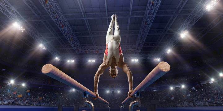 Male athlete doing a complicated exciting trick on parallel bars in a professional gym. Man perform stunt in bright sports clothes