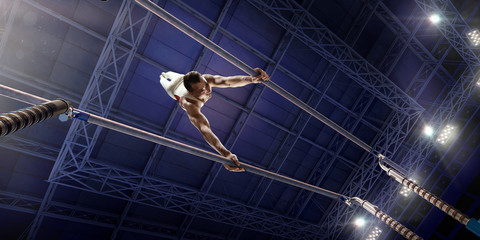 Male athlete doing a complicated exciting trick on parallel bars in a professional gym. Man perform...