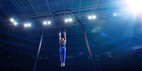 Male athlete doing a complicated exciting trick on gymnastics rings in a professional gym. Man perform stunt in bright sports clothes
