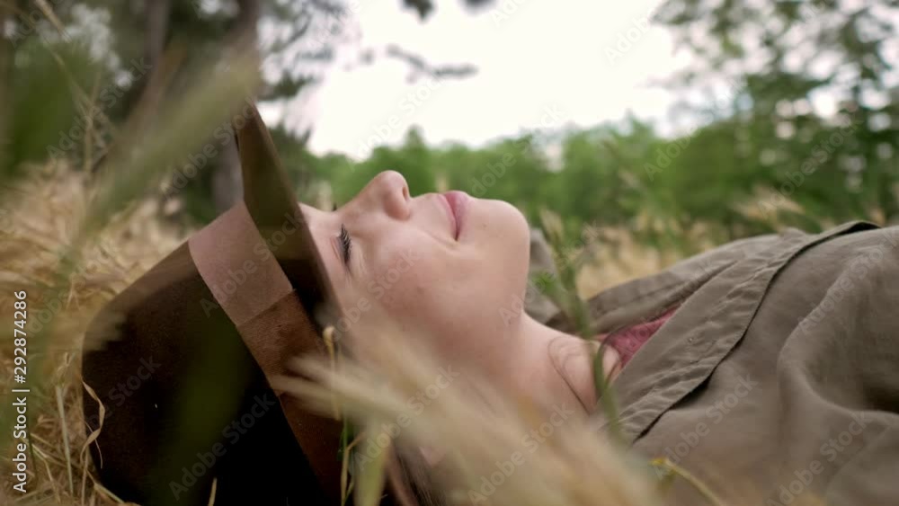 Canvas Prints Close up side view of calm cute young brunette woman in brown hat relaxing and smiling while lying on the grass in the park