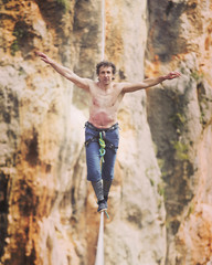 A man is walking along a stretched sling. Highline in the mountains. Man catches balance....