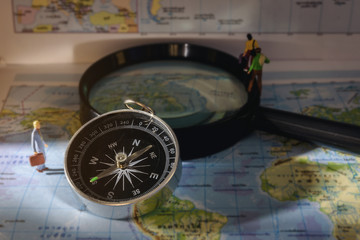 A compass that is used to travel with a magnifying glass and map that has a blurry background.