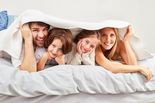 Eltern und Kinder verstecken sich unter Bettdecke