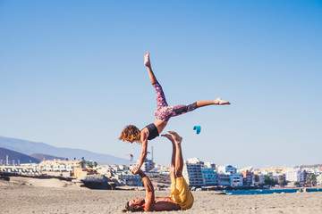 couple of adults in a friendship doing sports and activities like acroyoga at the beach on the sand with mountain at the background