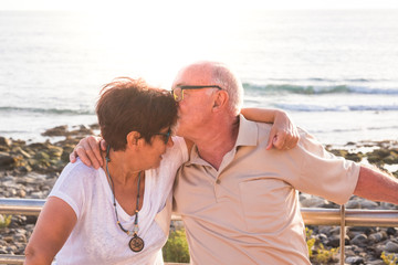 couple of seniors hogging at the beach with a lot of love - retired together - woman with glasses and man with sea background - kissing her