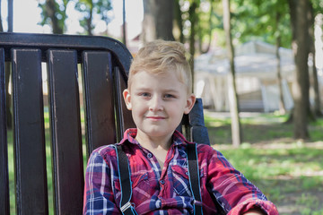 Beautiful boy 7 years old sits on a bench in the park.