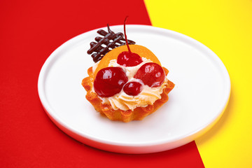 delicious cake, tartlet in a basket with whipped cream, decorated with berries, fruits and chocolate on a white plate. On a bright color background