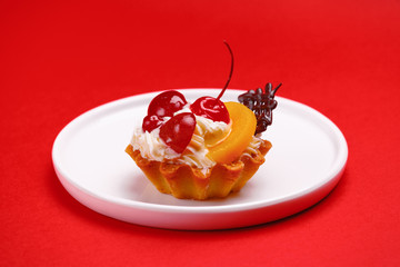 delicious cake, tartlet in a basket with whipped cream, decorated with berries, fruits and chocolate on a white plate. On a bright color background
