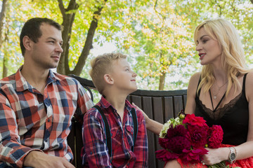 Young family sitting on a bench in a park.