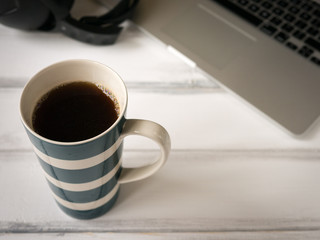 White wooden working desk with notebook, headphones and large mug of cofee. Shallow depth of field.