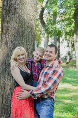 Beautiful happy young family hugs by a tree in the park.