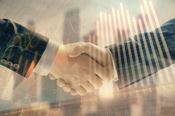 Double exposure of financial graph on cityscape background with two businessman handshake. Concept...