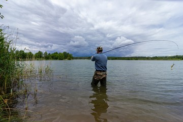 fisherman standing in the lake and catching the fish during cloudy day