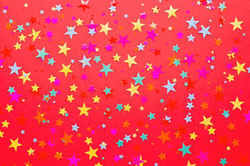 Festive red background with multicolor star confetti and streamers. Background for birthdays, christmas, anniversary
