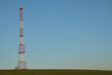 Communications tower at the blue sky background and green meadow