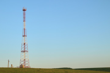 Communications tower at the blue sky background and green meadow