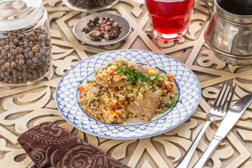 pilaf with chicken on white plate and glass of red drink on oriental wooden table
