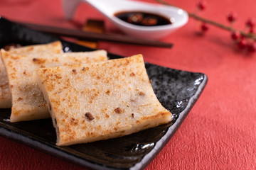 Chinese lunar new year food concept, Delicious turnip radish cake, local cuisine in restaurant with soy sauce on red background, close up, copy space