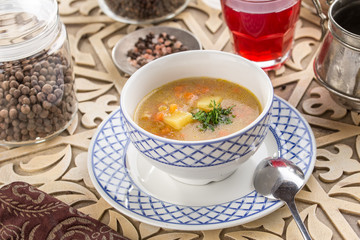 homemade vegetable soup with potatoes garnished with parsley and glass of red drink on oriental wooden table