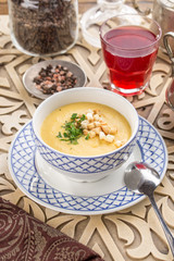 vegetable soup with pumpkin and croutons and glass of red drink on oriental wooden table