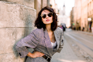 Trendy fashion woman in jacket and sunglasses walking on the street, urban city scene. Copy space - obrazy, fototapety, plakaty