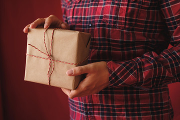 Man in plaid shirt holding Christmas box Gift on red background. Male hands with Presents for winter Holidays. Christmas, New Year, shopping, preparation on Holidays concept. Close up