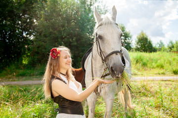Beautiful caucasian young girl walking with a horse and enjoys summertime in countryside.