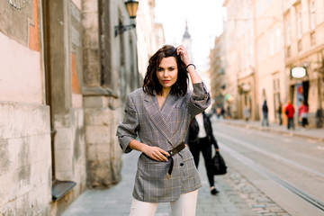 Fototapeta premium Elegant business woman wearing stylish jacket and white pants at summer day morning in the city street