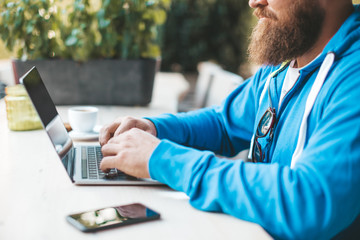 Image of young bearded man sitting in a cafe with cup of coffee, using pc at the table - business...