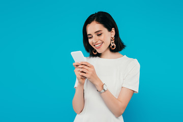smiling elegant woman in dress using smartphone isolated on blue