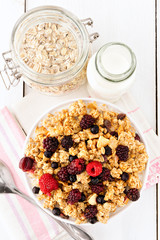 Healthy breakfast. Bowl of fresh muesli with colorful berry fruits, on top of white, wooden breakfast table. Overhead view.